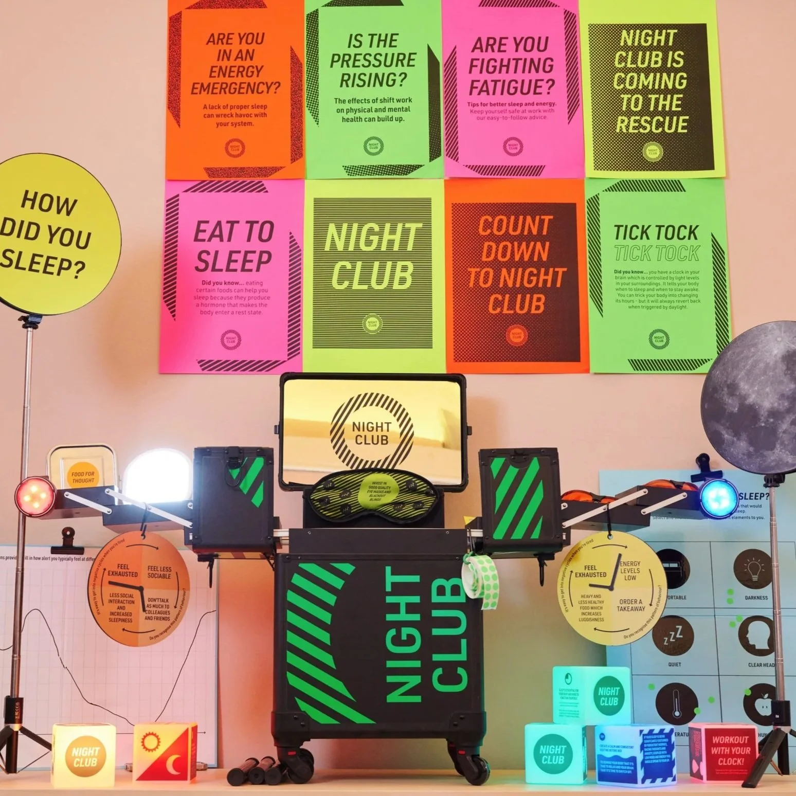 A display about sleep and night clubs featuring colorful posters with questions and facts, a moon-shaped lamp, and various devices and signs related to sleep, energy, and nighttime activities.