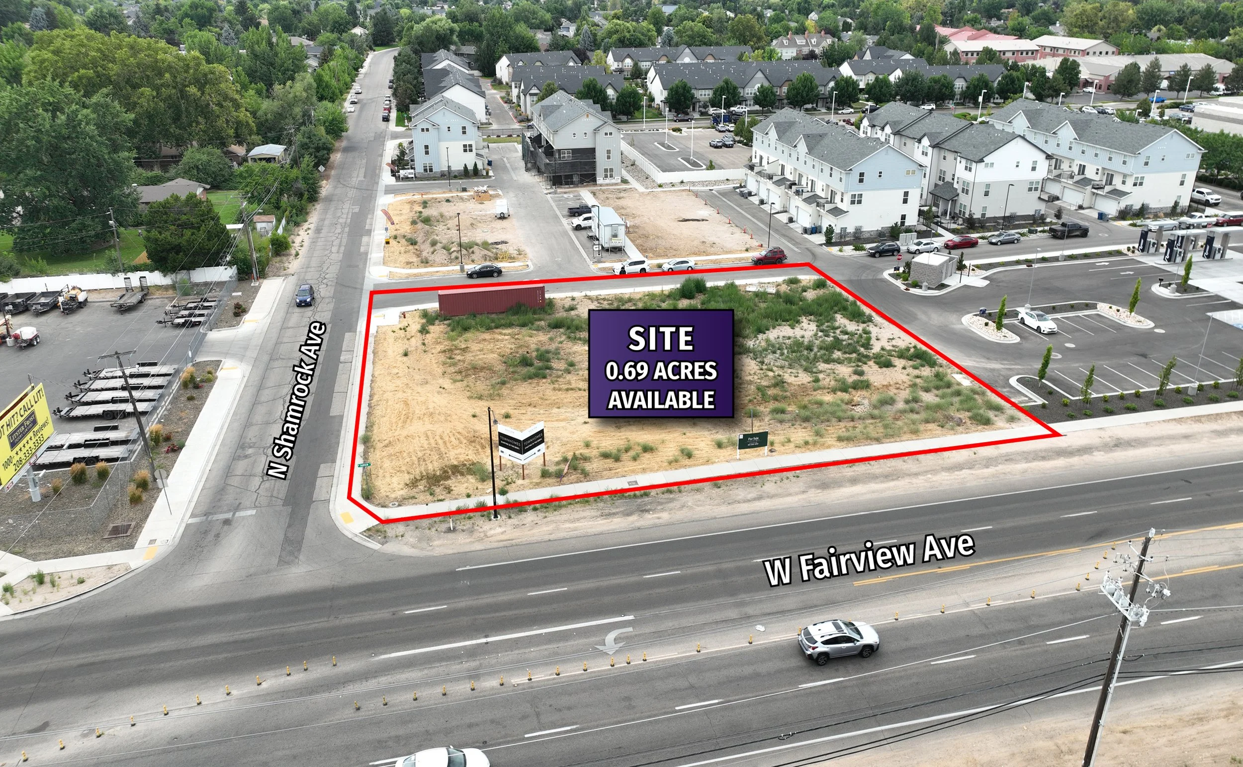A vacant lot outlined in red located at the intersection of North Shamrock Avenue and West Fairview Avenue, with a sign indicating 0.69 acres available for sale or development, surrounded by residential buildings, a parking lot, and a gas station.