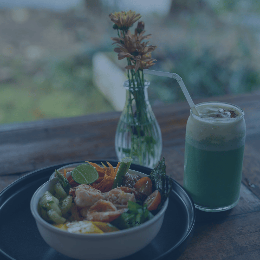 A bowl of shrimp and vegetables next to a vase of orange flowers and a green drink
