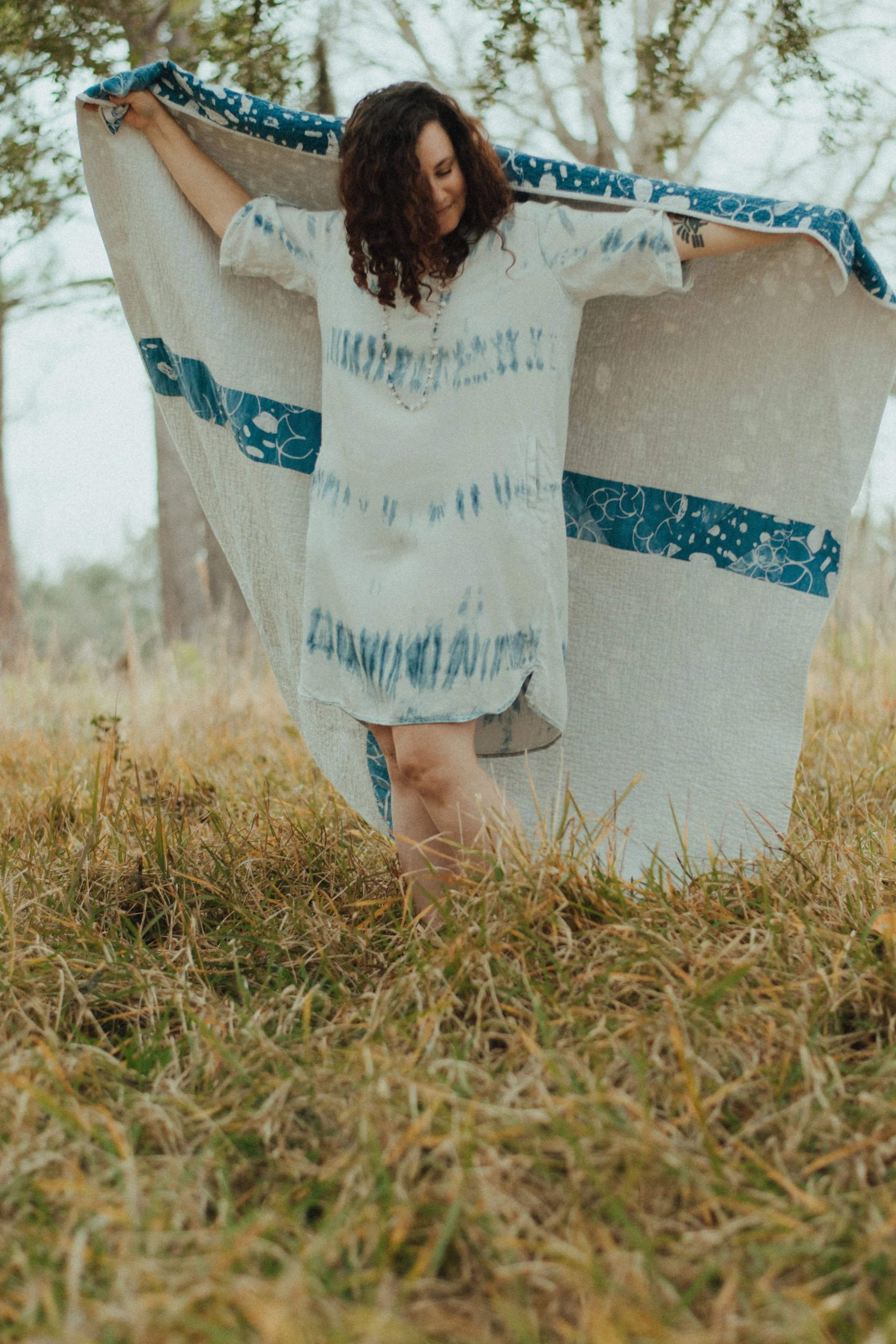 Textile artist Kate Reuschel holding a hand dyed indigo shibori fabric outdoors. Founder of Dyes Happy, creating original wallpaper and fabric designs inspired by hand dyeing, watercolor, and nature.