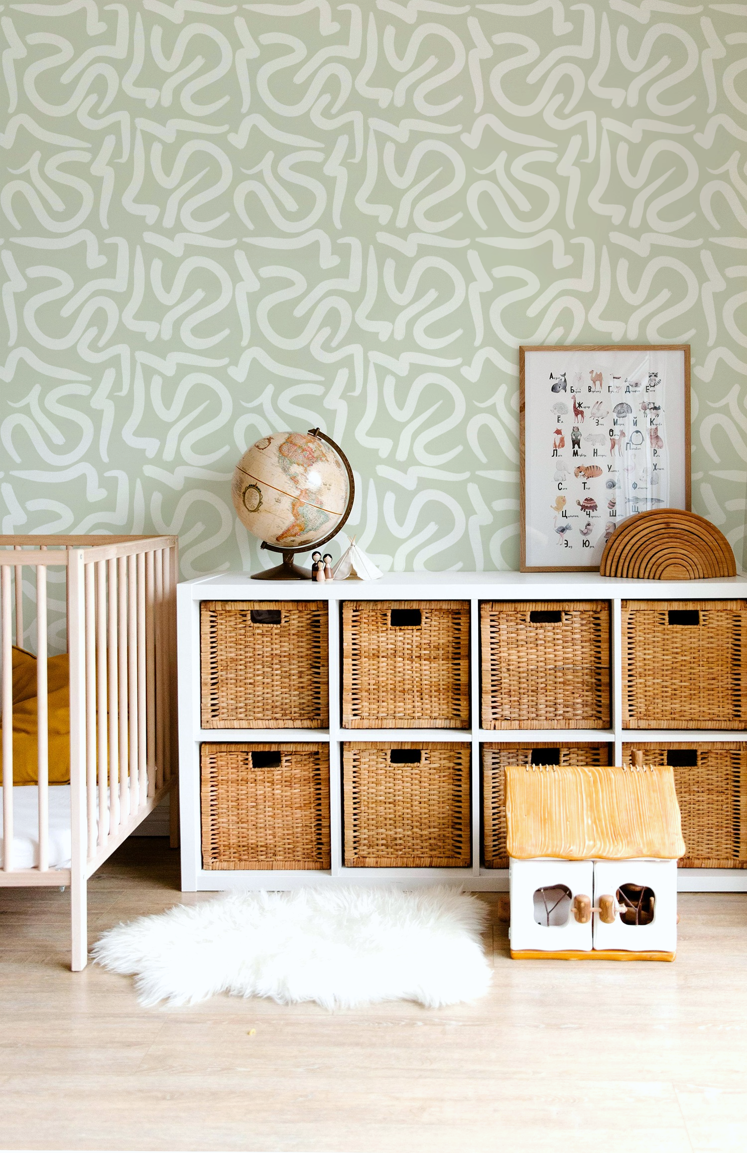 Original hand painted abstract geometric wallpaper in soft sage green displayed in a modern nursery with natural wood furniture.