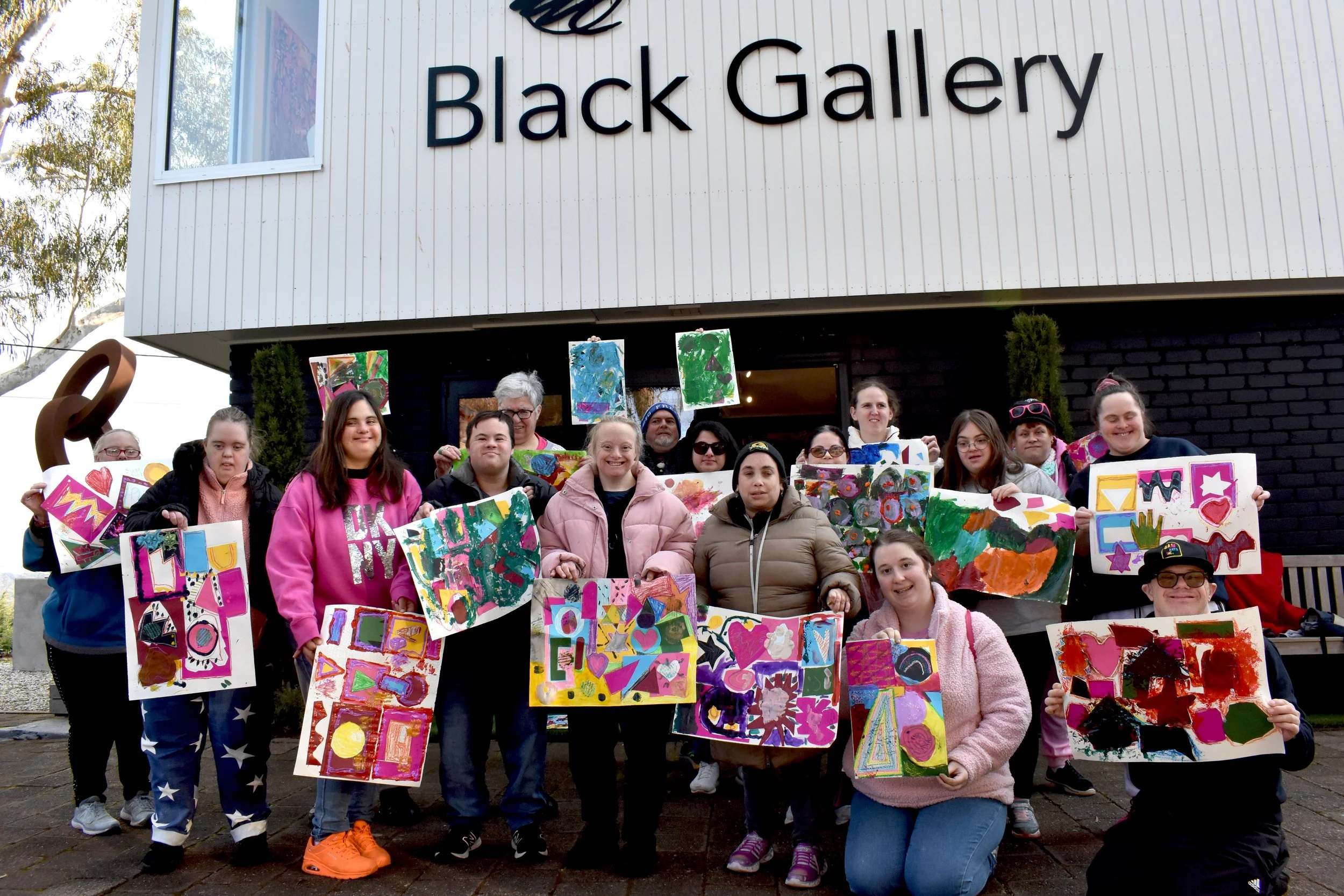 A group of children and adults holding colorful painted posters in front of the Black Gallery building.