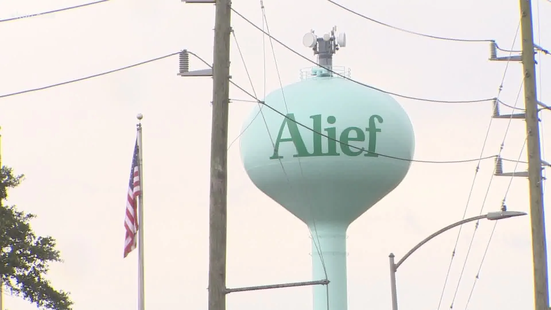 Alief water tower in Houston with American flag, power lines, utility poles, and streetlight on a cloudy day