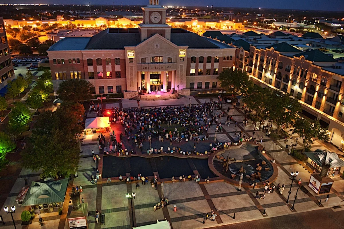 Aerial view of a public gathering at a city square in front of a lit civic building during an evening event.