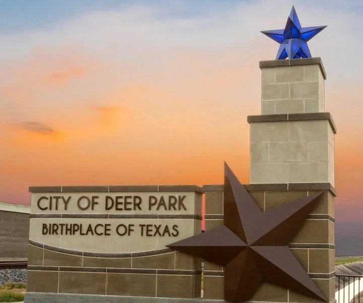 City of Deer Park monument sign with star sculptures and stone columns against a colorful sunset sky backdrop.