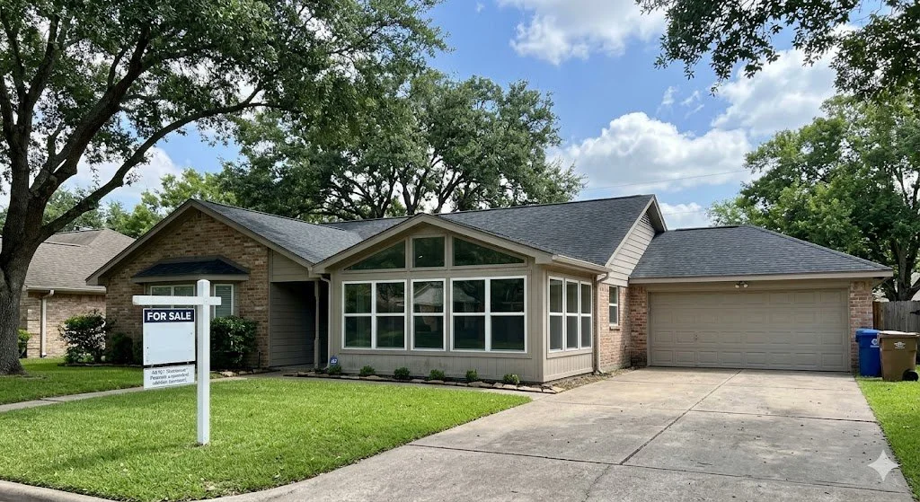 A Houston home for sale featuring a sunroom addition and a real estate sign on a sunny day with green trees.