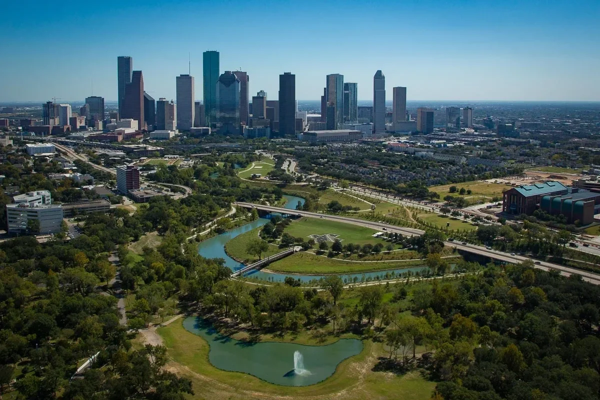 Aerial view of downtown Houston skyline and Buffalo Bayou Park with green spaces, bridges, and city skyline on clear day.