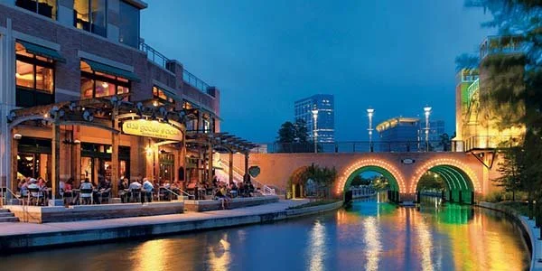 The Woodlands Waterway at night with restaurants, lit bridge arches, and reflections on canal water in Texas.