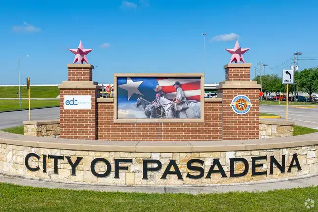 City of Pasadena Texas entrance sign with brick monument, Texas flag mural, and star sculptures along roadway.