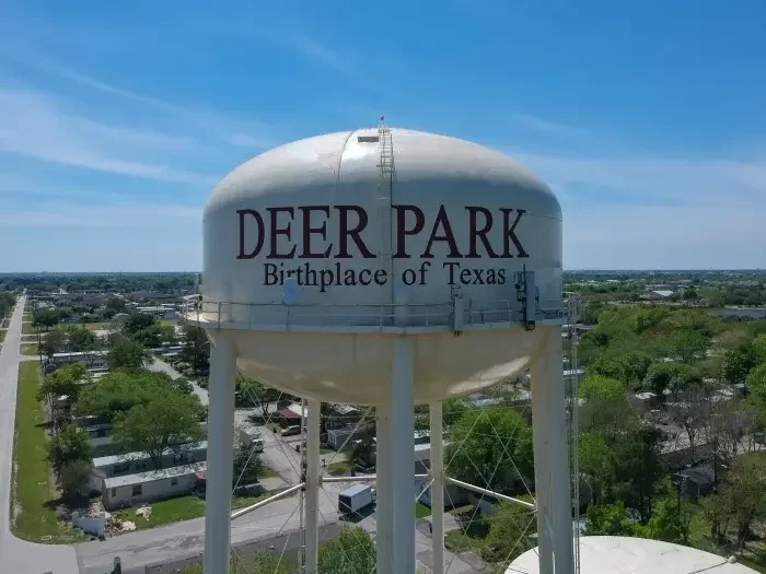 Deer Park Texas water tower with “Birthplace of Texas” text, aerial view over nearby neighborhood and trees on clear day.