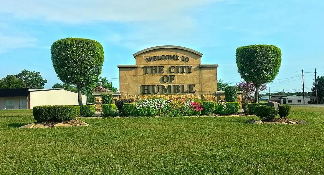 Welcome to the City of Humble monument sign surrounded by trimmed hedges, flowers, and a grassy landscape.