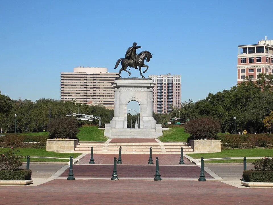 Sam Houston monument in Hermann Park Houston with statue on arch pedestal and city buildings in background.