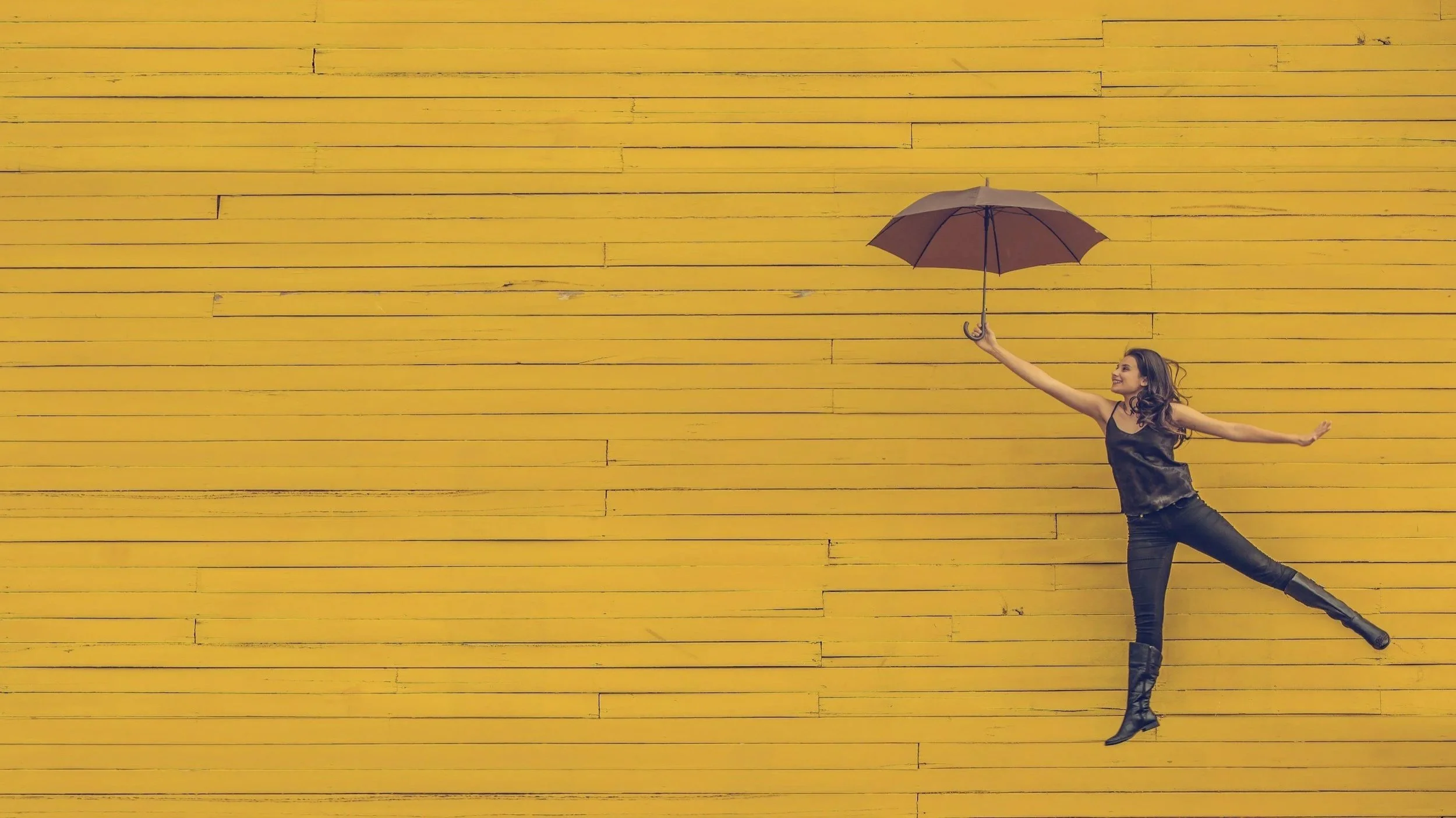 A dancer holding a red umbrella, appearing as though they are floating against a background of yellow planks