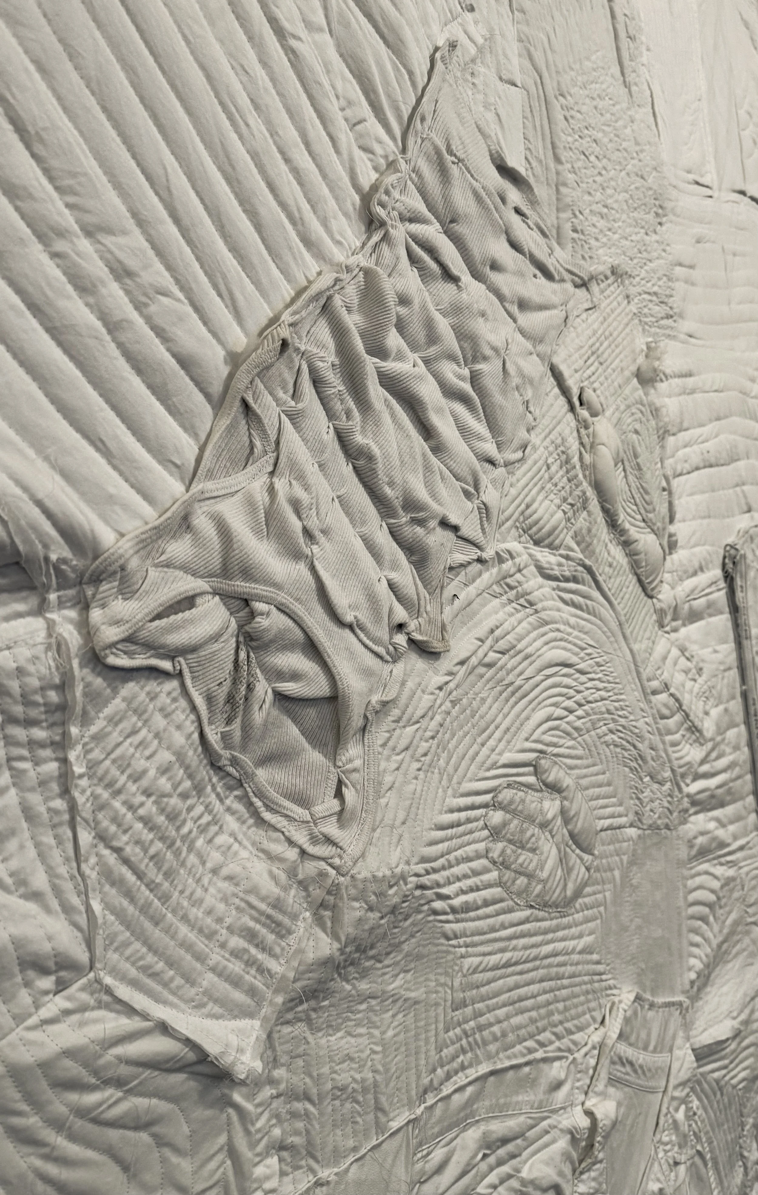 Cream-colored quilted bedspread with a matching ruffled pillow on a bed.