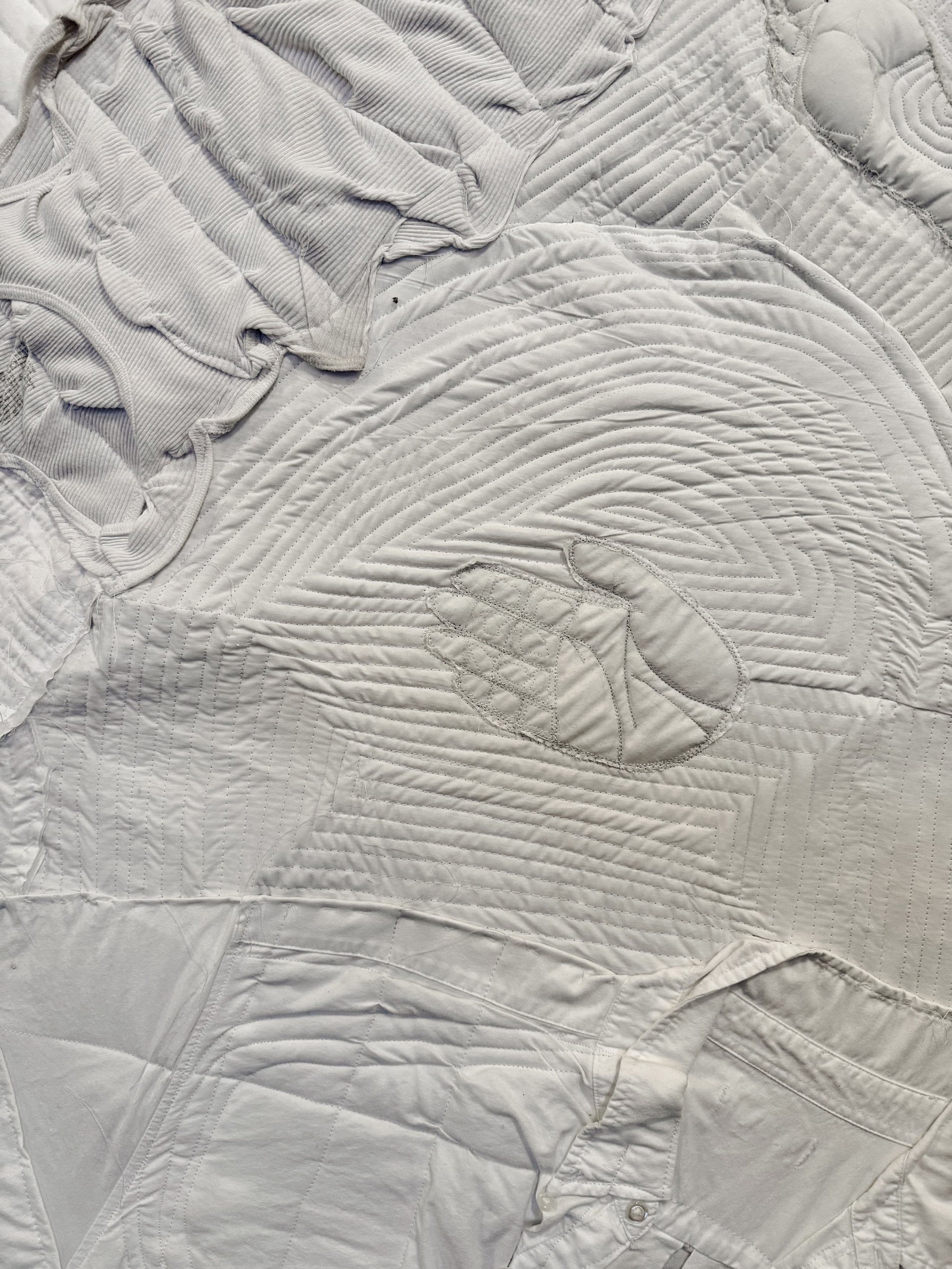 Close-up of white quilted fabric with stitched design resembling a mountain landscape and a stylized animal, possibly a bear or a fox.
