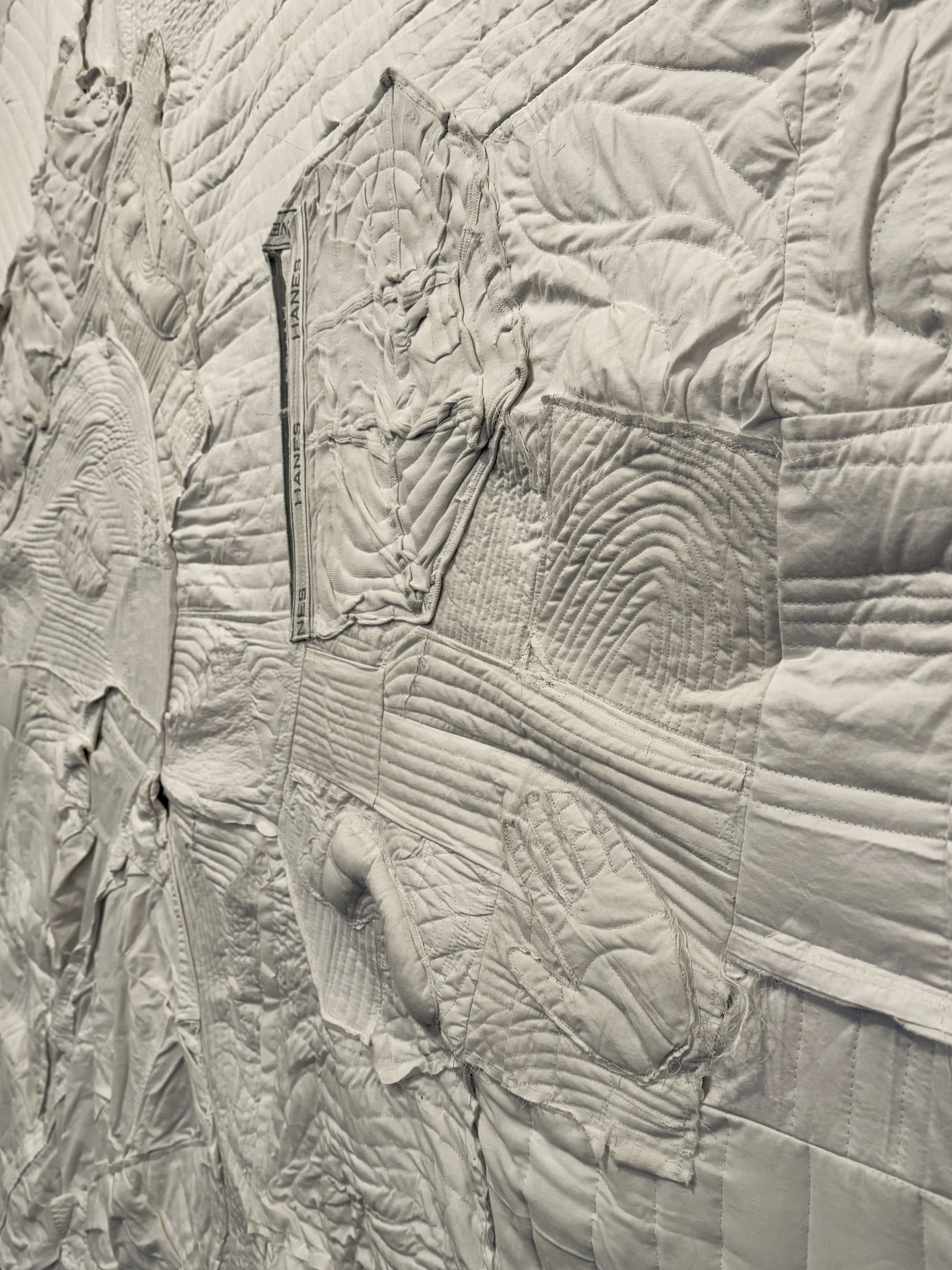 Close-up of a textured, quilted white fabric with stitched patterns, zippers, and a glove design.