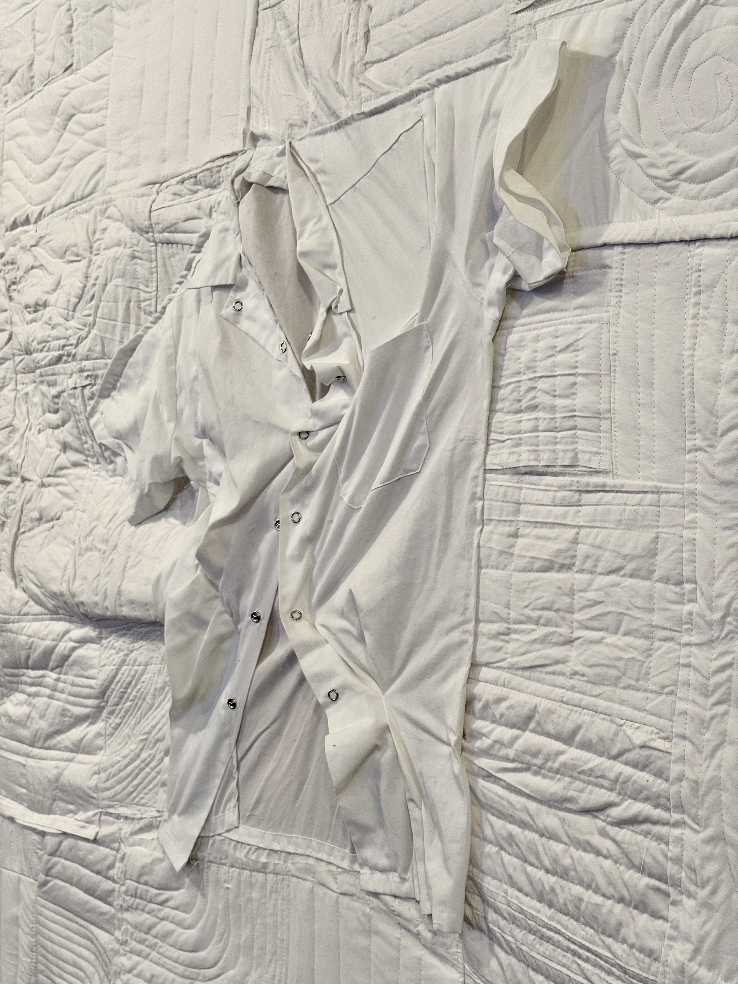 A crumpled white satin sheet or bedsheet with a satin shirt on top, lying on a textured white bedspread.