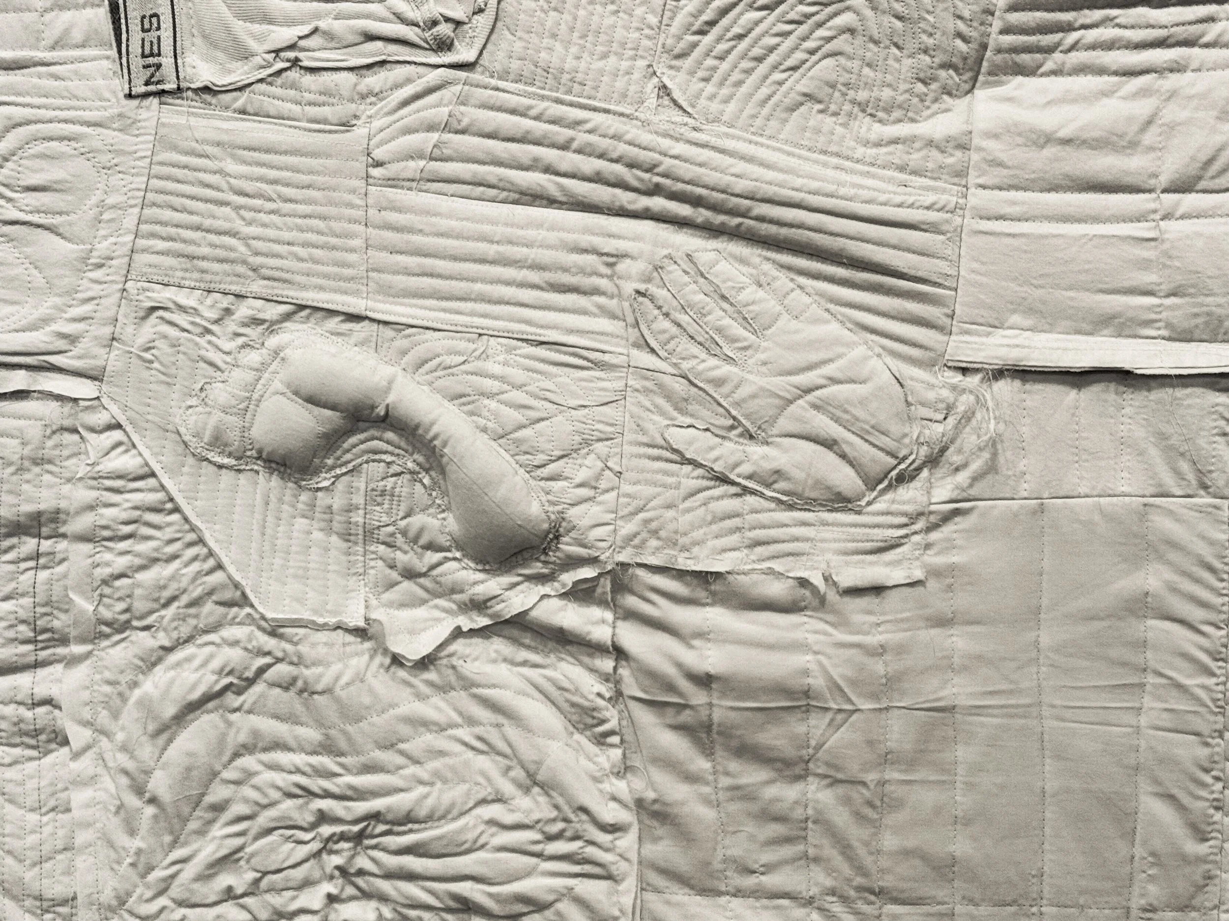 A quilted white fabric with patterns resembling a hand holding a hammer and a hand holding a screwdriver.