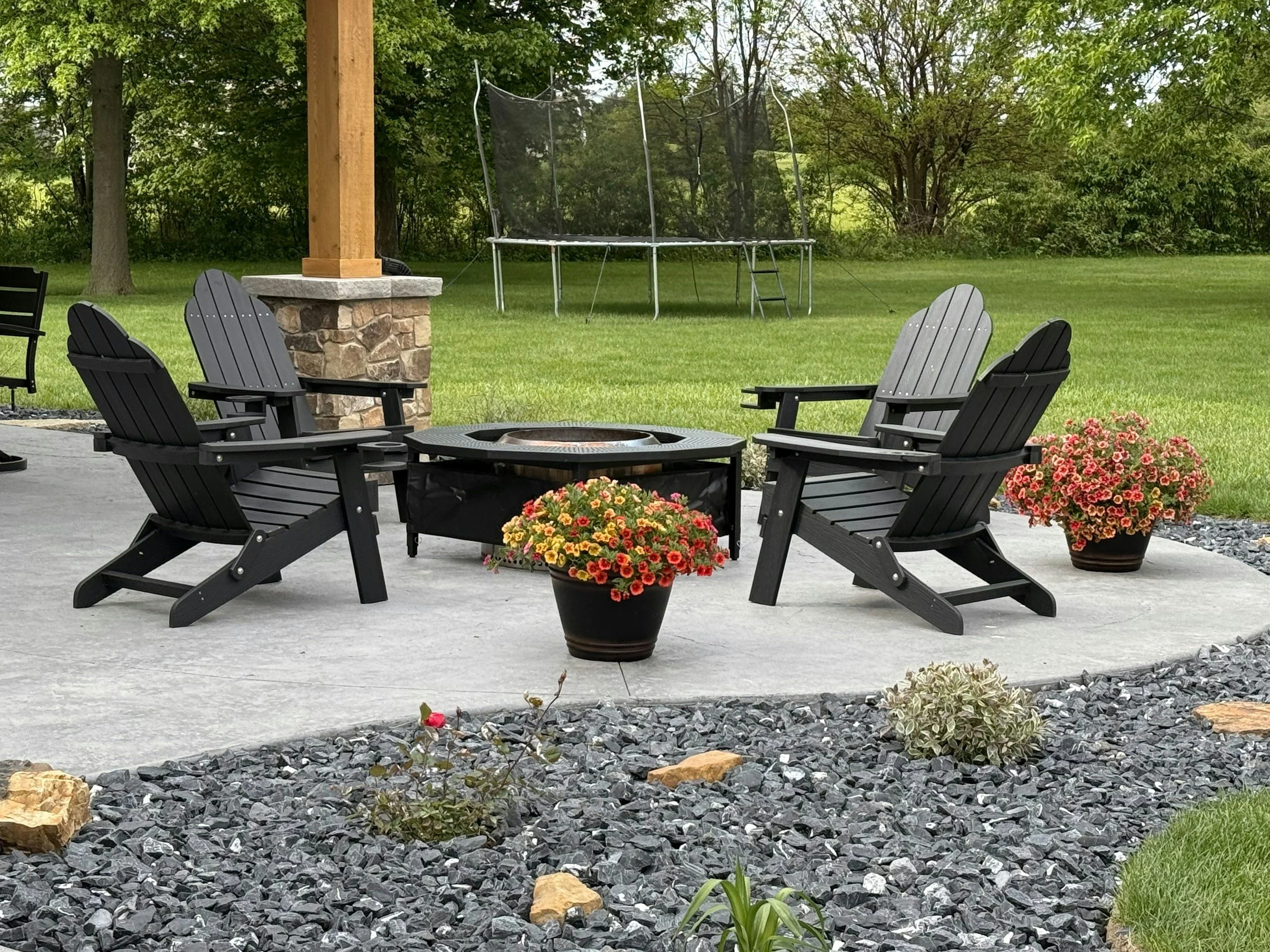 backyard patio with black adirondack chairs surrounding a fire pit and a trampoline in the backgroundin Wilmette IL