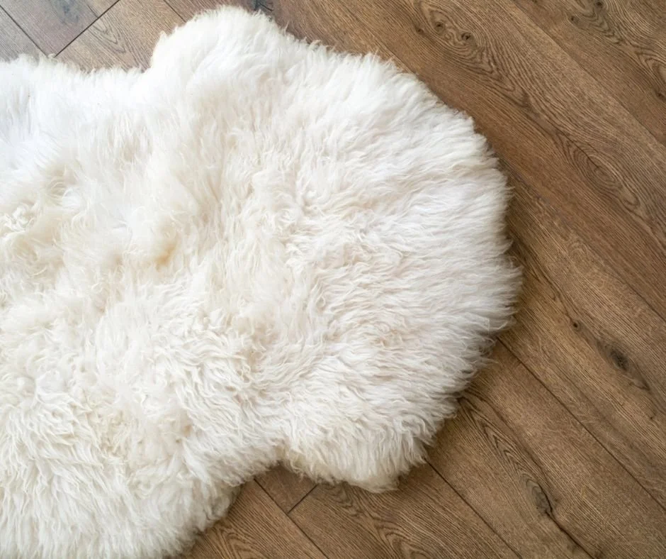 A white fluffy sheep skin rug on a medium tone wood floor