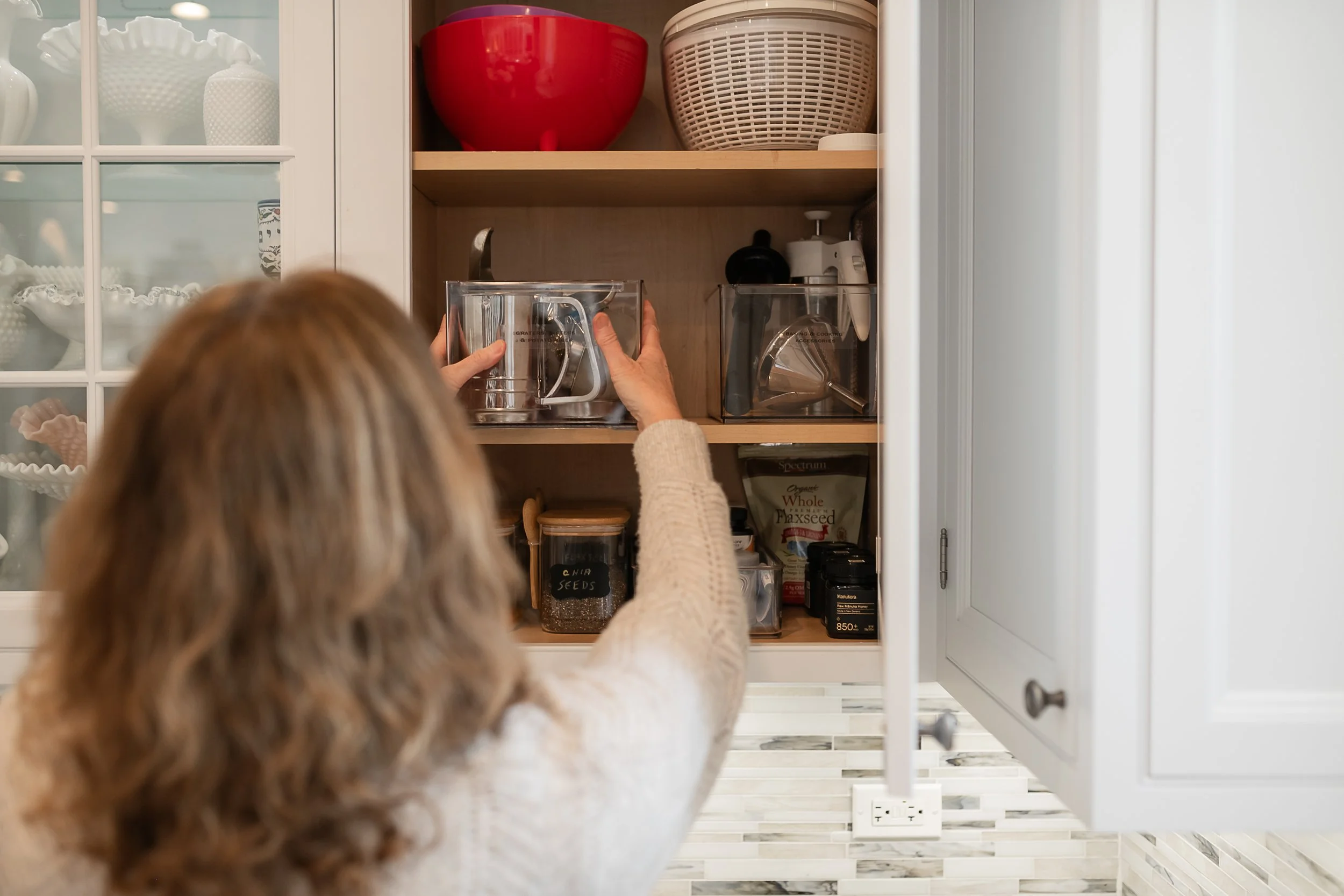 Organizer placing a bin in a kitchen cabinet for organization purposes.
