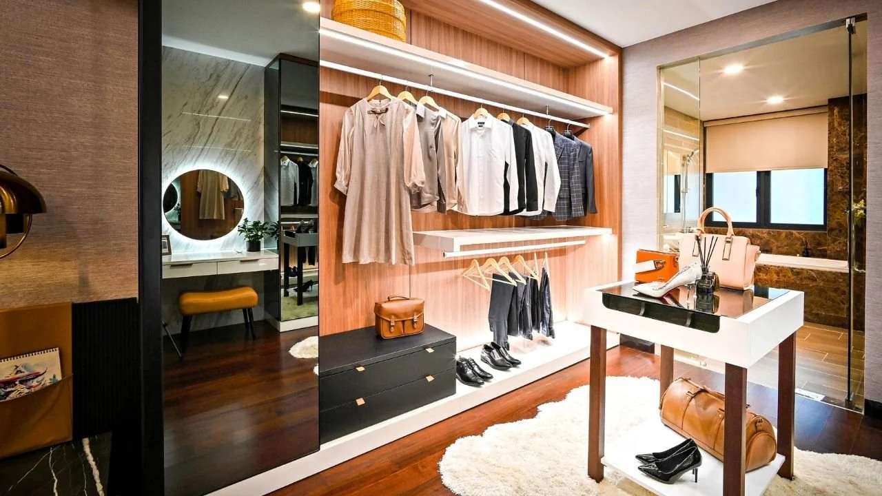 A built in master closet filled with minimal clothing on hangers including a dress, button up shirts, and pants folded. The interior of the closet it well lit and has a sliding mirrored door.