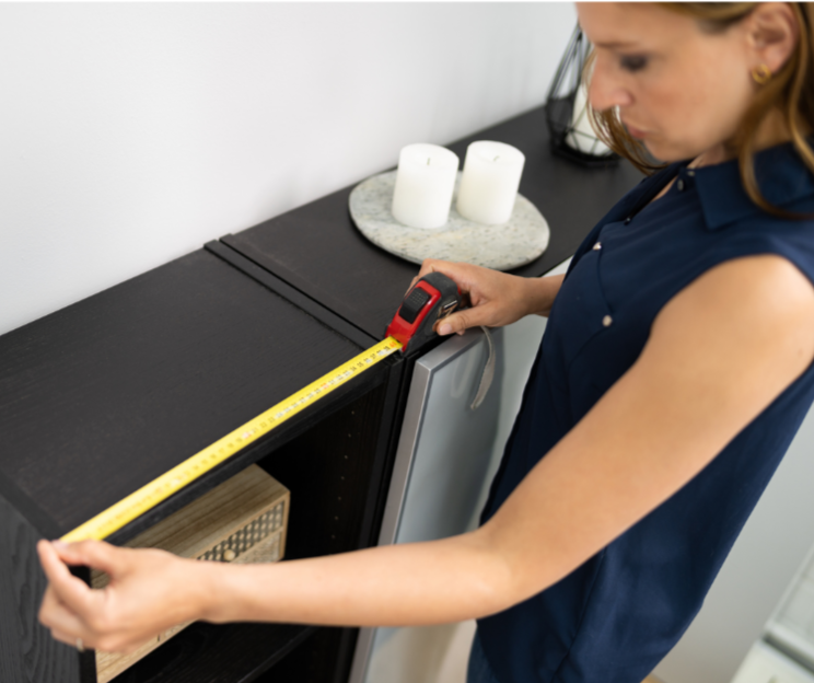Woman measuring the width of a black bookcase with a tape measure in a modern room.