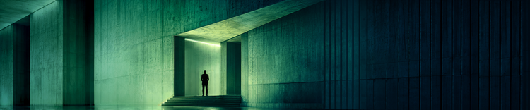 Lone figure standing at an illuminated green doorway in massive angular architecture