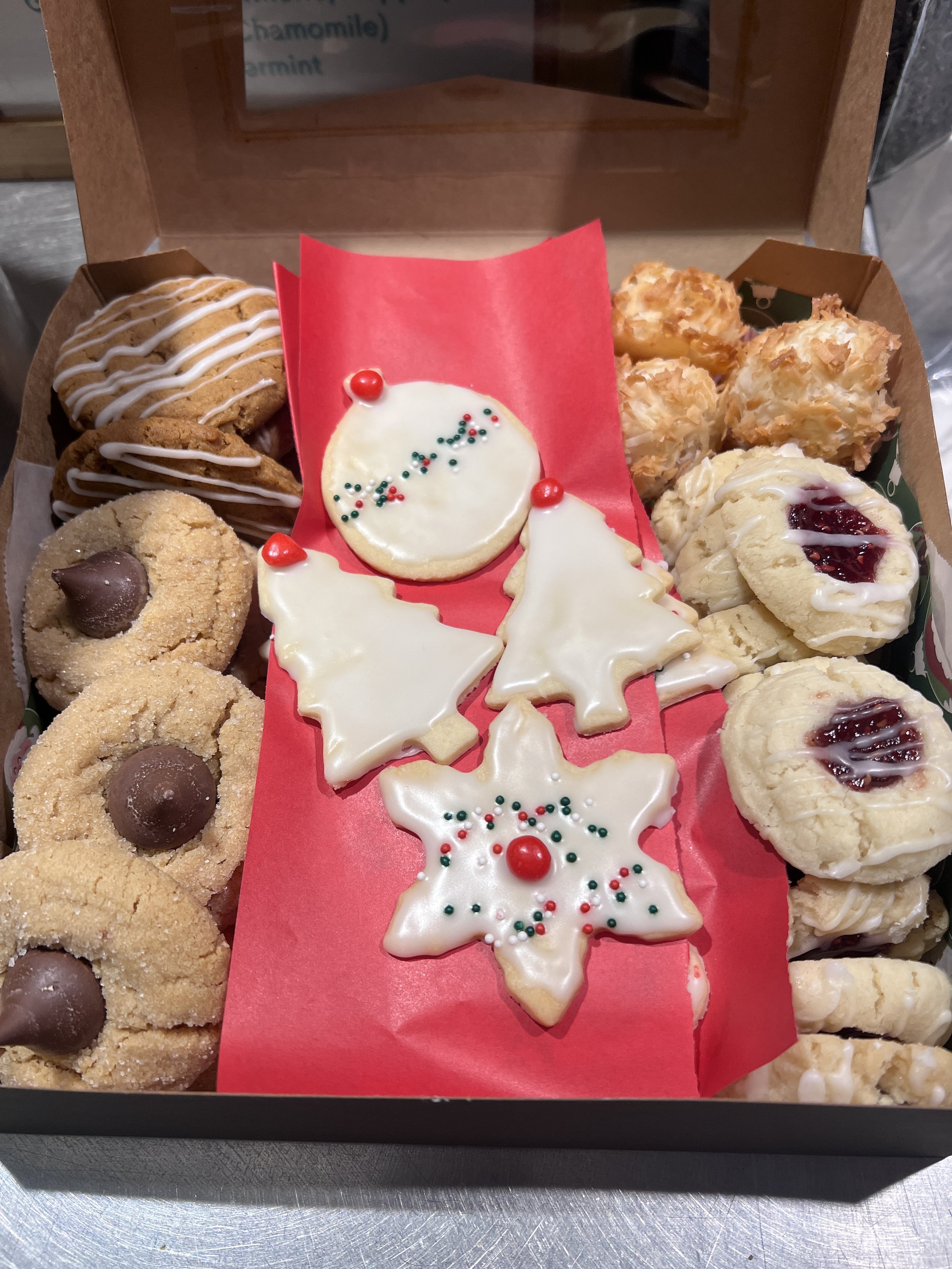 Assortment of homemade holiday cookies in a bakery box from SiP Coffeebar in Northeast Minneapolis, including decorated sugar cookies, peanut butter blossoms, and raspberry thumbprints.