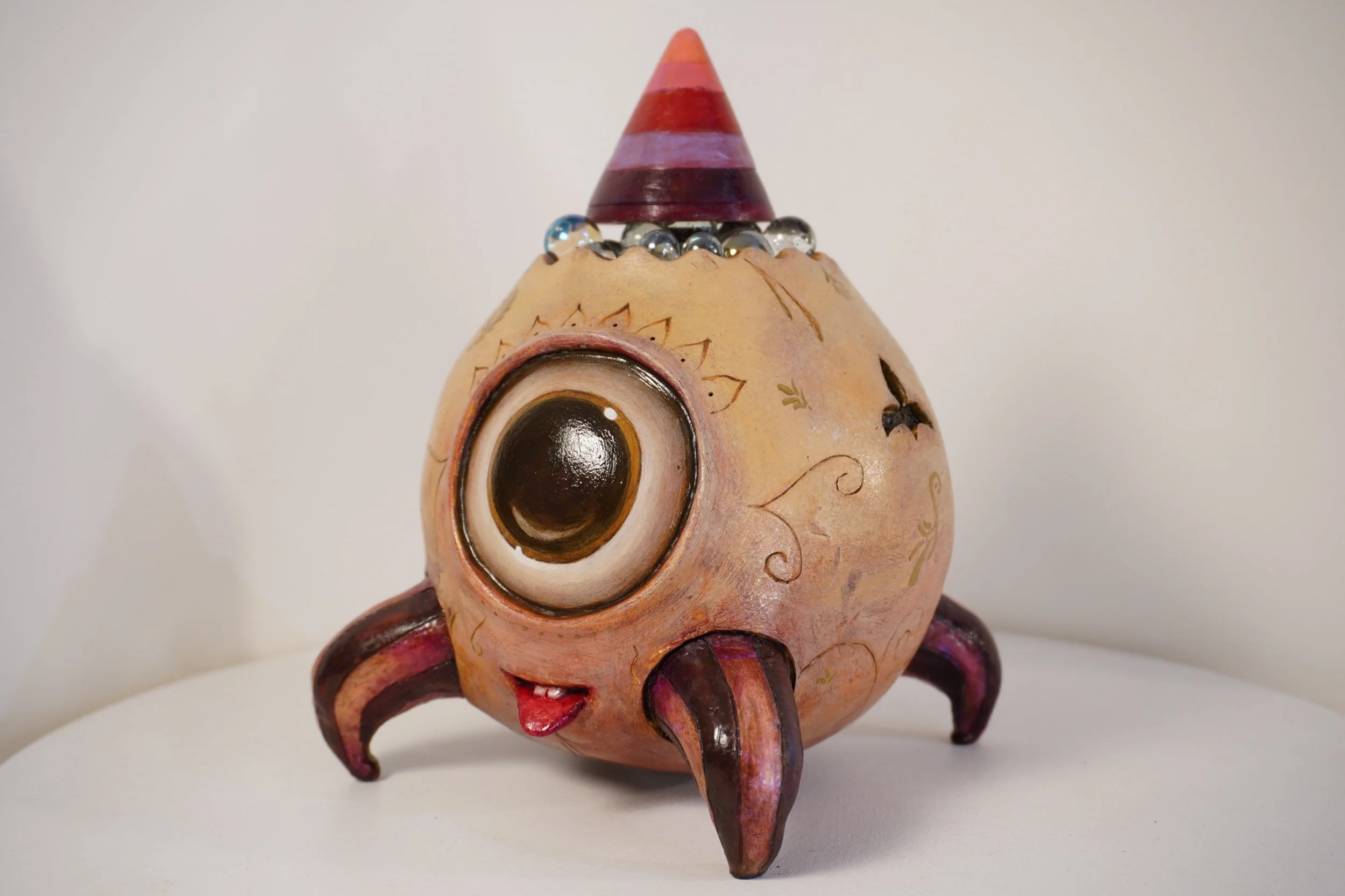 A decorative sculpture of an abstract creature with a large eye, multiple legs, and a cone-shaped structure on top, painted in earthy and reddish tones with painted details.