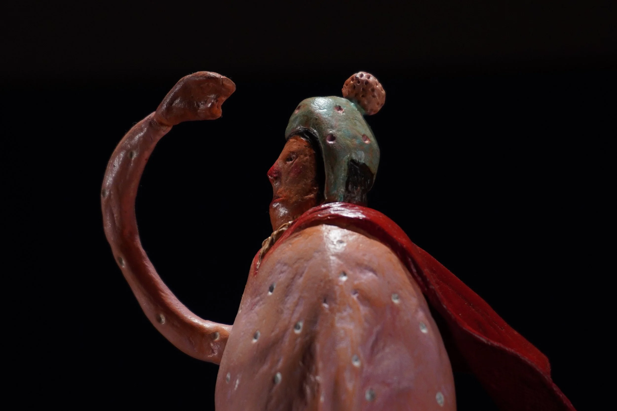 Close-up of a sculpture resembling child made of airdry clay with rusted and weathered textures, set against a black background.