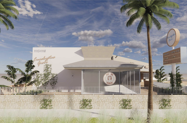 Modern building with a white exterior, surrounded by palm trees and a stone wall, under a partly cloudy sky.
