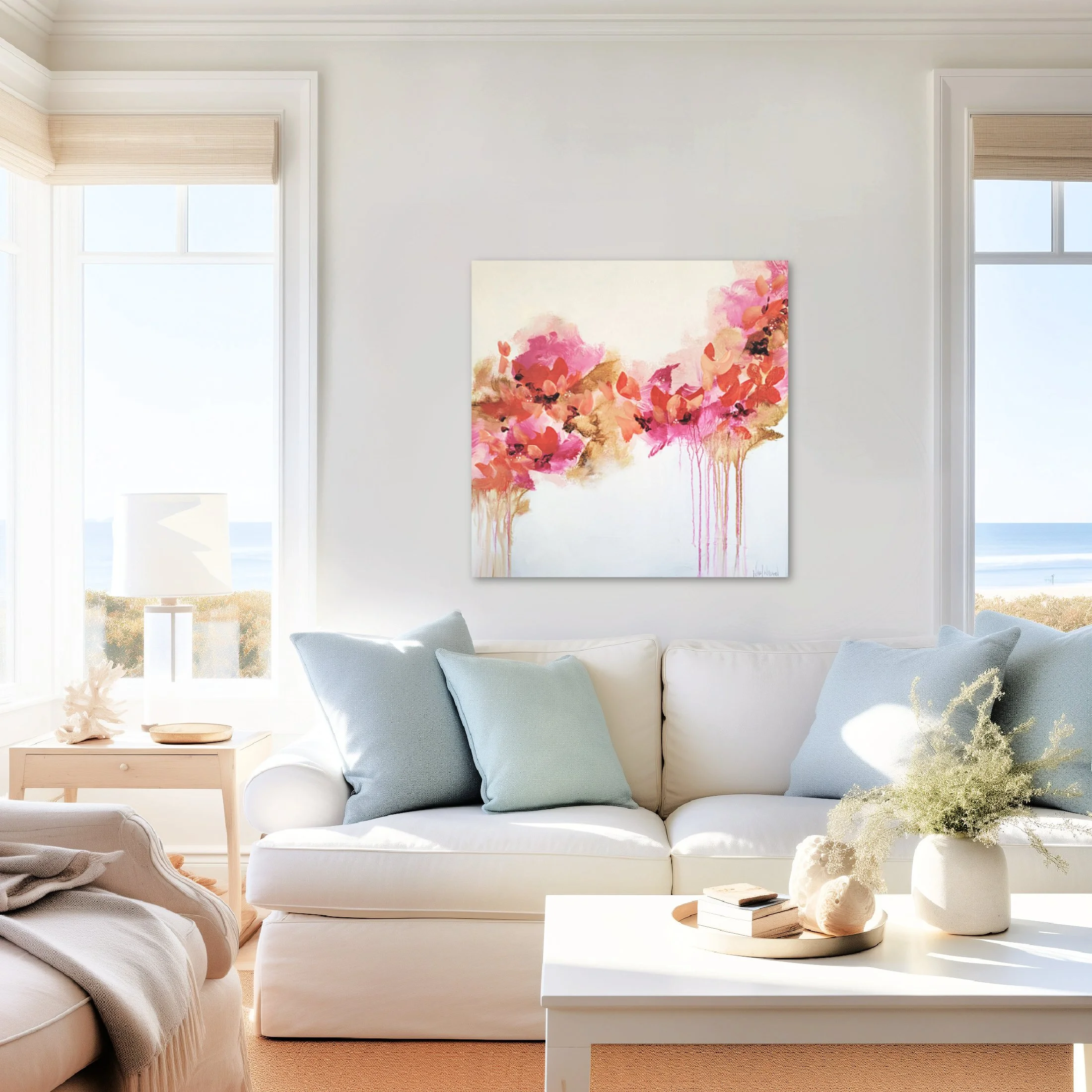 Living room with white sofa, pastel blue cushions, a white coffee table with decorative objects, an abstract floral painting on the wall, large windows with blinds, and a view of an open landscape outside.