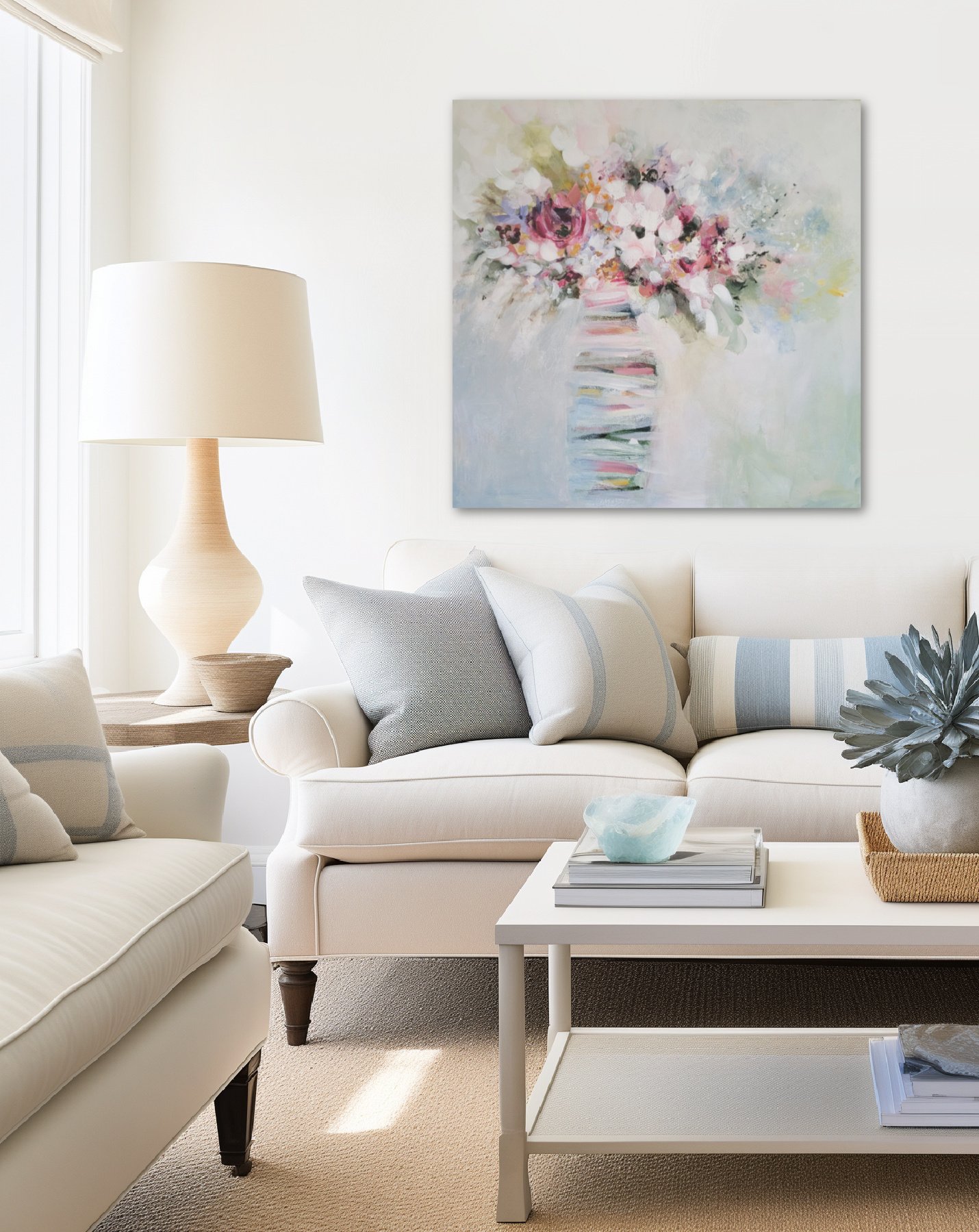 Living room with white sofa, pillows, glass table with decor, large floral painting by Nikol Wikman, and lamps, in natural sunlight.