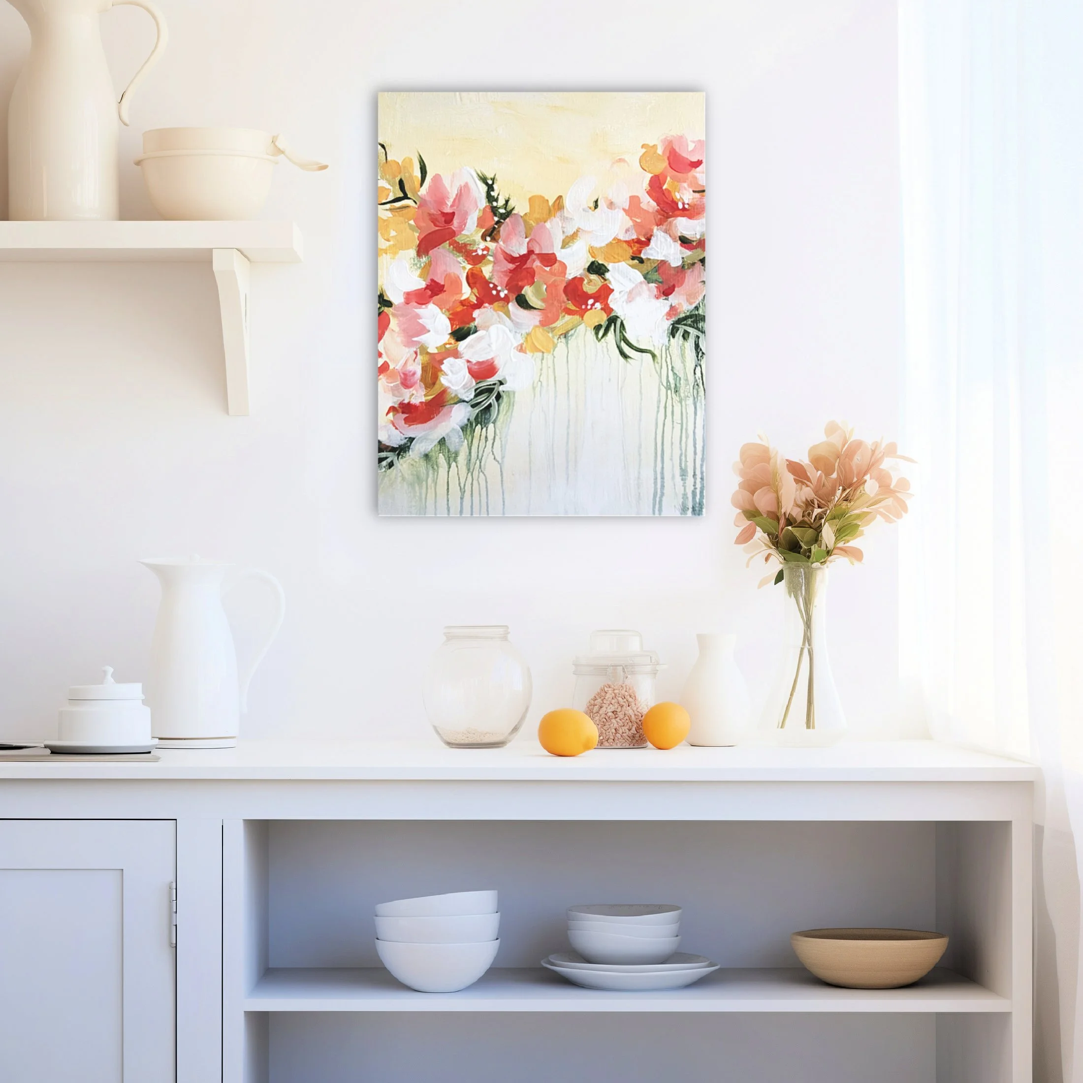 A white kitchen shelf displaying white and cream ceramic pitchers and bowls, with a colorful abstract floral painting and a vase of pinkish flowers on a white surface.