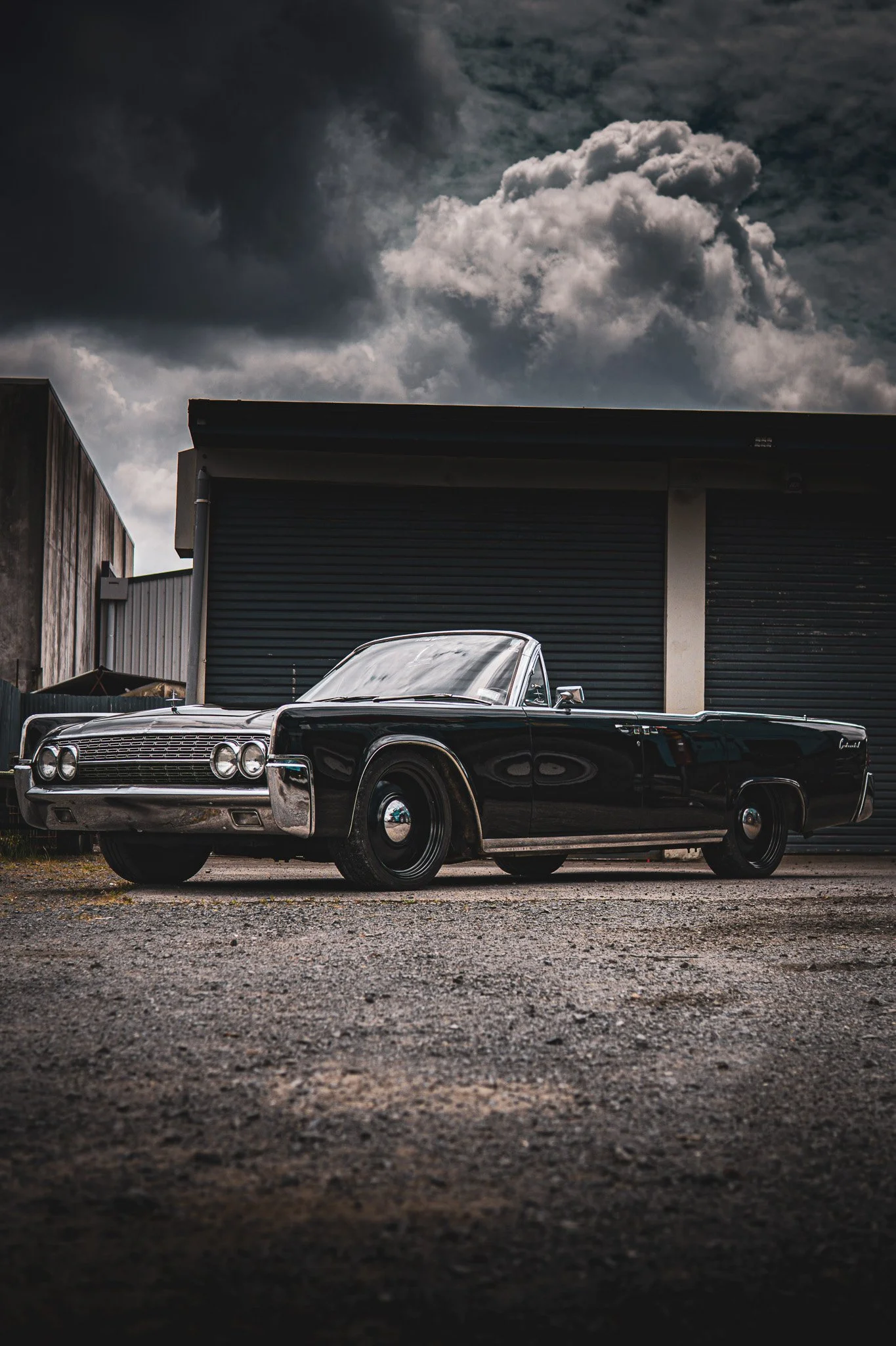 A vintage Lincoln  black car parked outdoors against a building with a cloudy sky overhead.