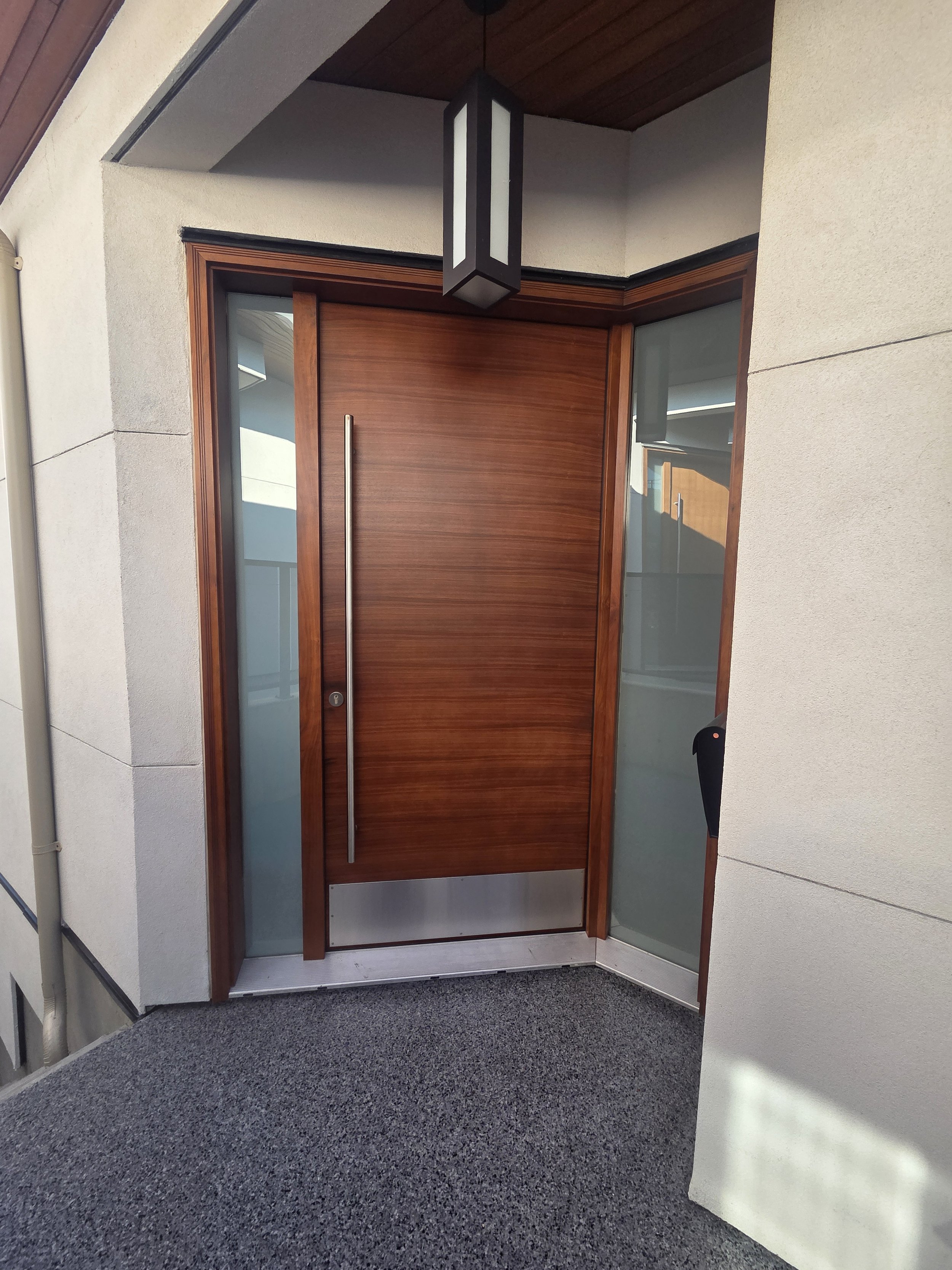 Wood entry door with a long metal pull and glass sidelights.