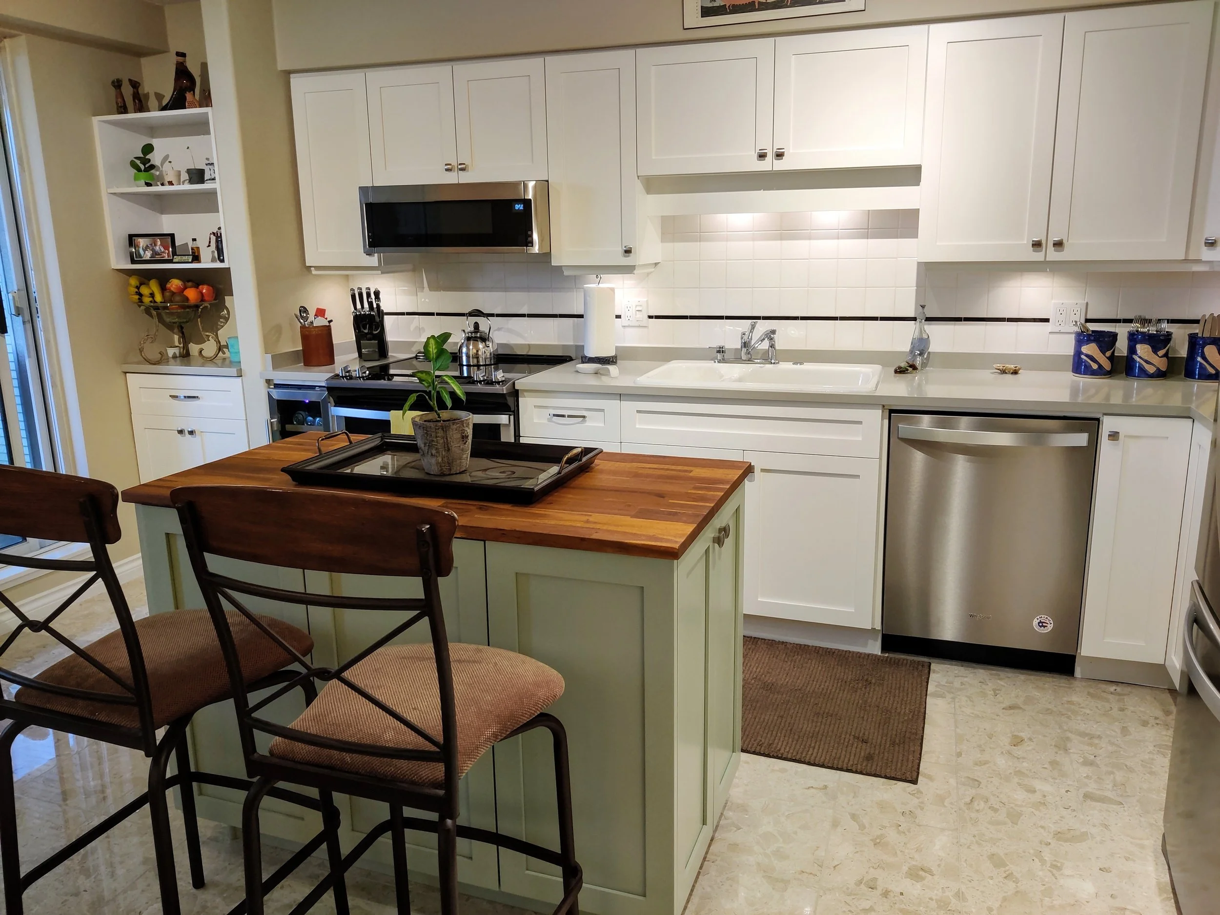 White shaker kitchen with a sage island and wood countertop.