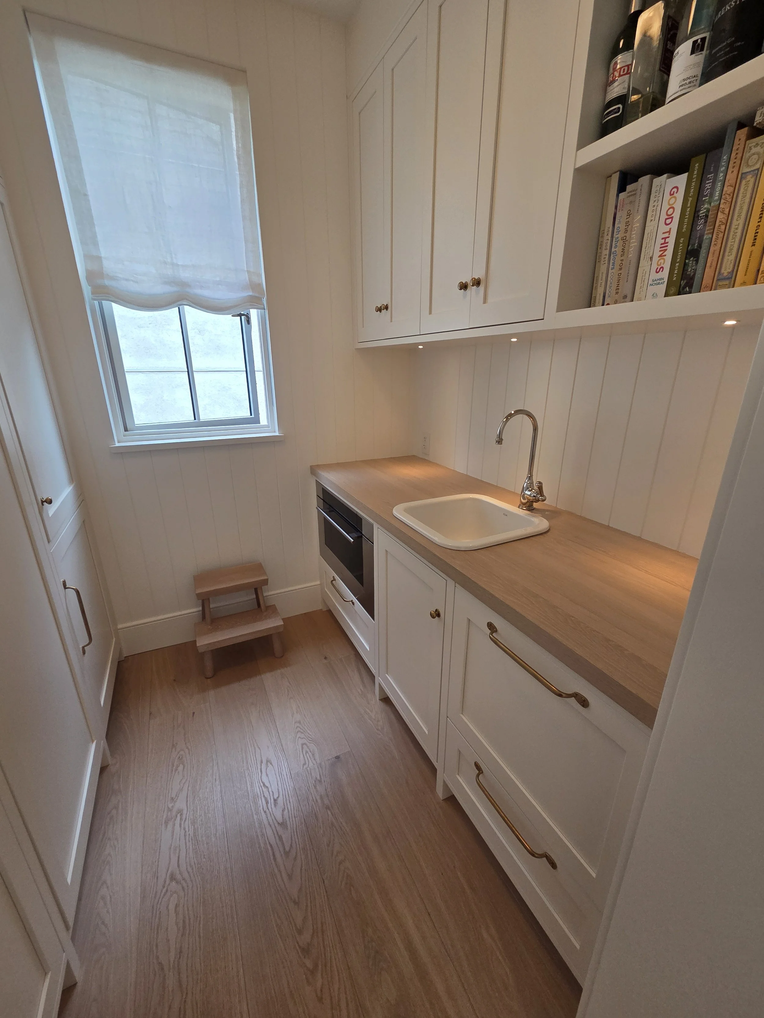 Butler’s pantry with white cabinetry, wood counters and brass pulls.