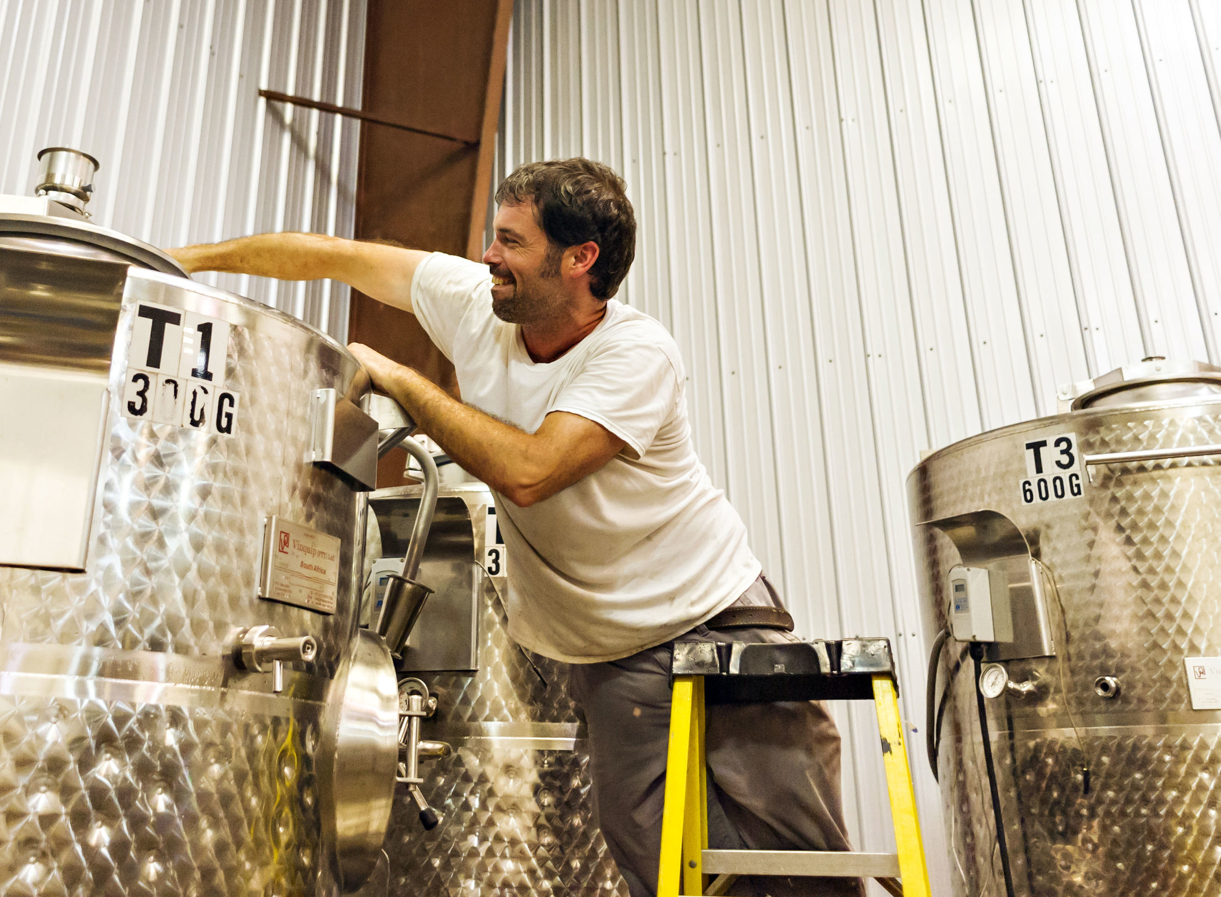 A wine maker at Sanctuary Vineyards leans into a steel tank to punch down the grapes. 