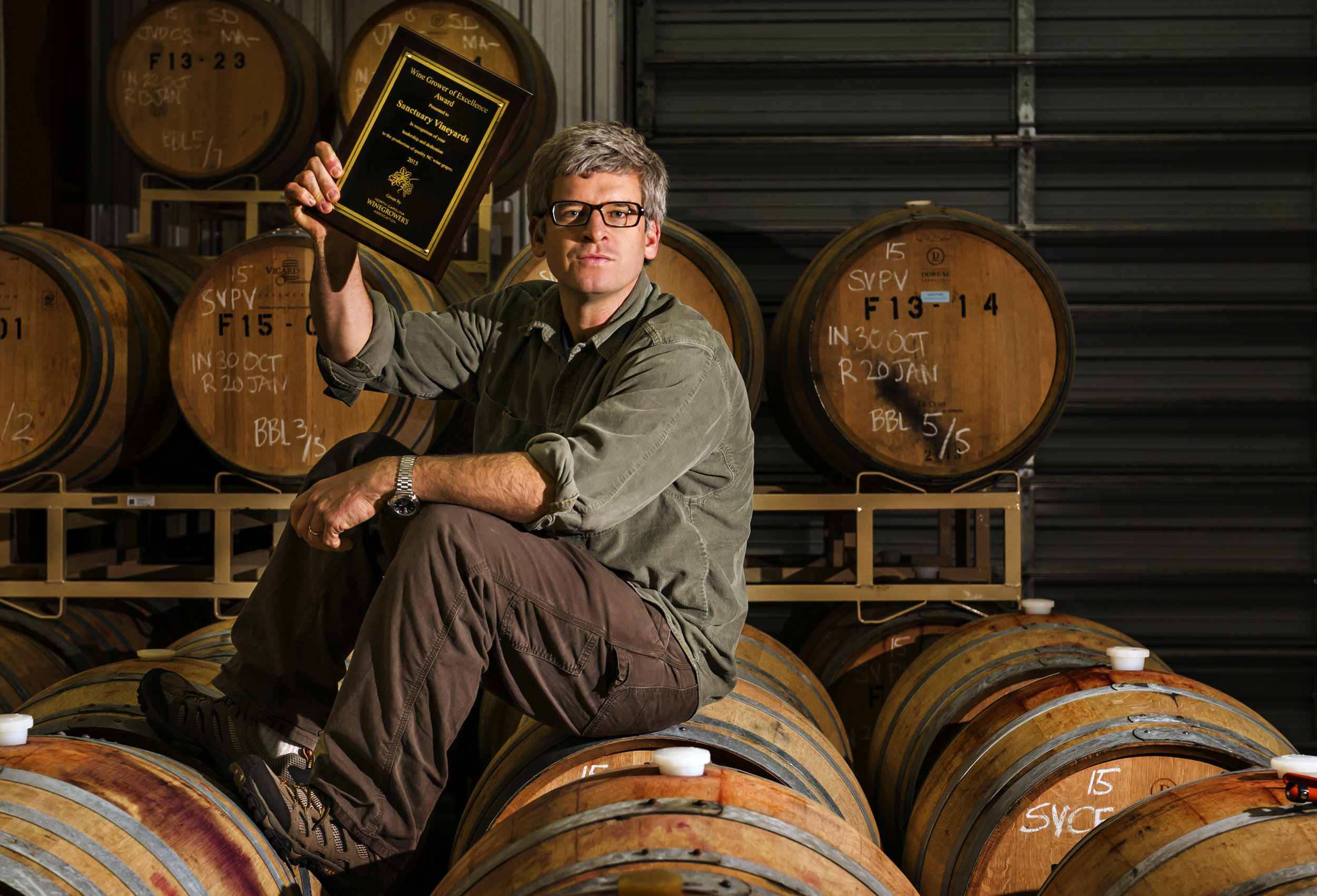 Outer Banks winemaker sits on a wine barrel showing off his award for Best of Wines. 