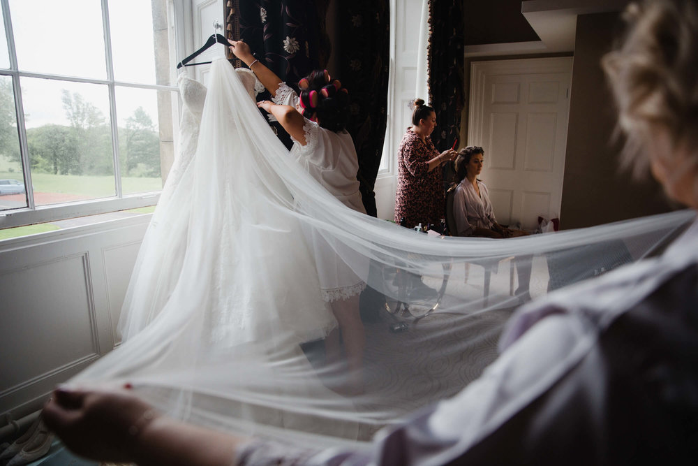 bridesmaid holding wedding dress veil for bride during wedding preparation