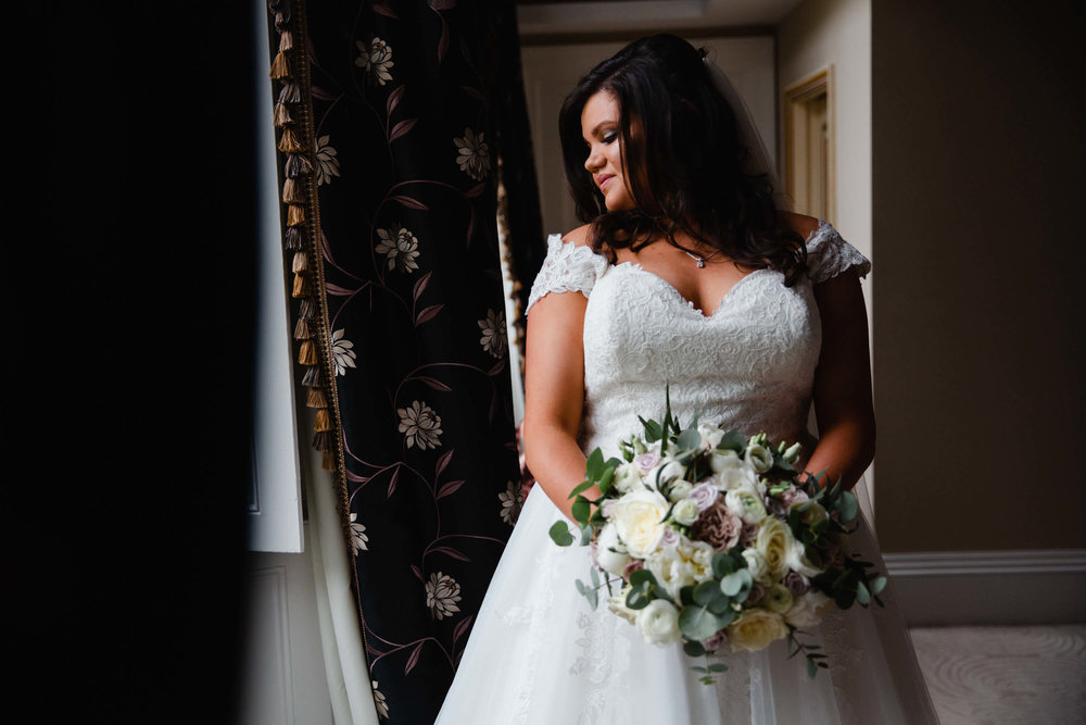 portrait of bride in window holding bouquet of flowers at haigh hall