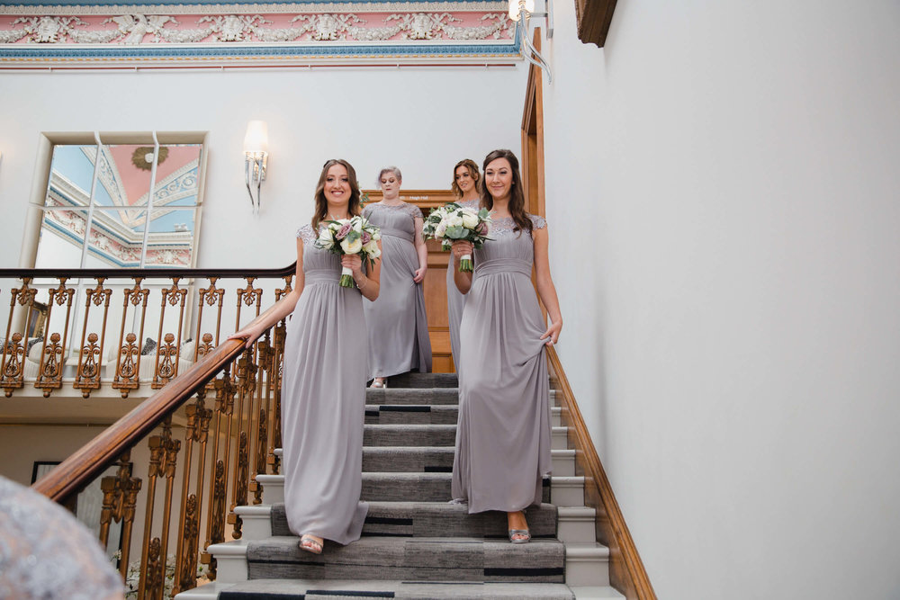 bridesmaids holding bouquets walking down staircase on way to ceremony