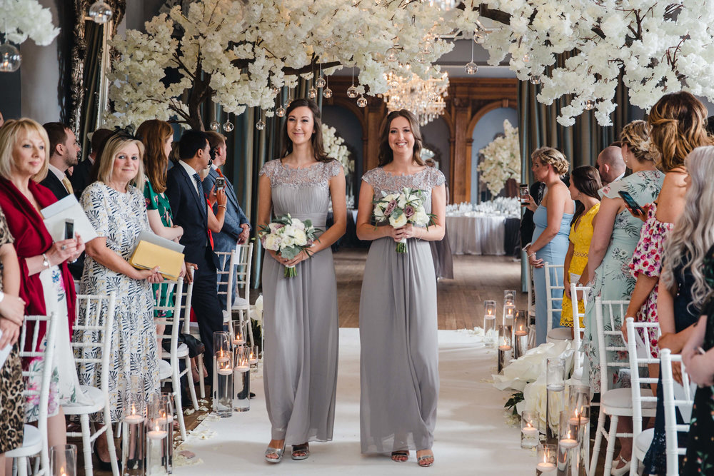 bridesmaids walking down ceremony aisle under blossom trees