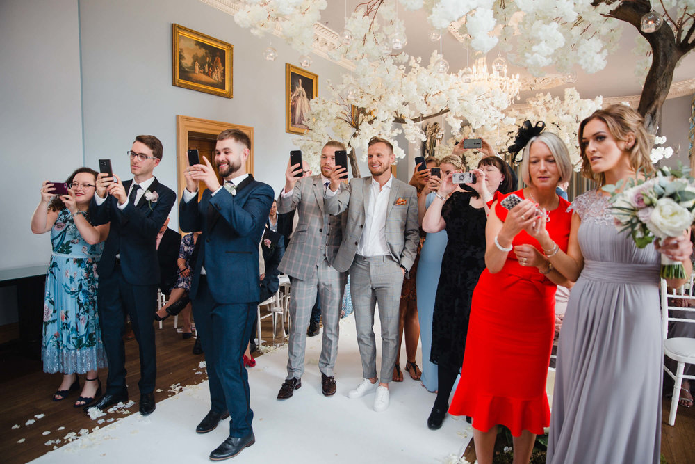 bridal party take photographs of newly wedded couple
