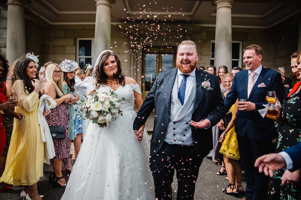 bride and groom run through confetti throwing from wedding party