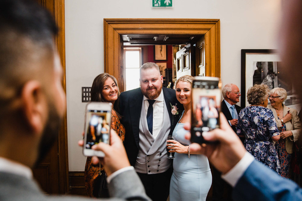 groom with wedding guests pose for camera phones during drinks reception