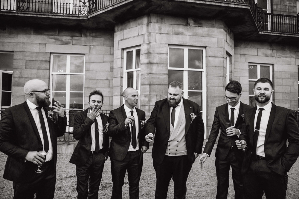 black and white photograph of groomsmen smoking cigars in gardens of haigh hall