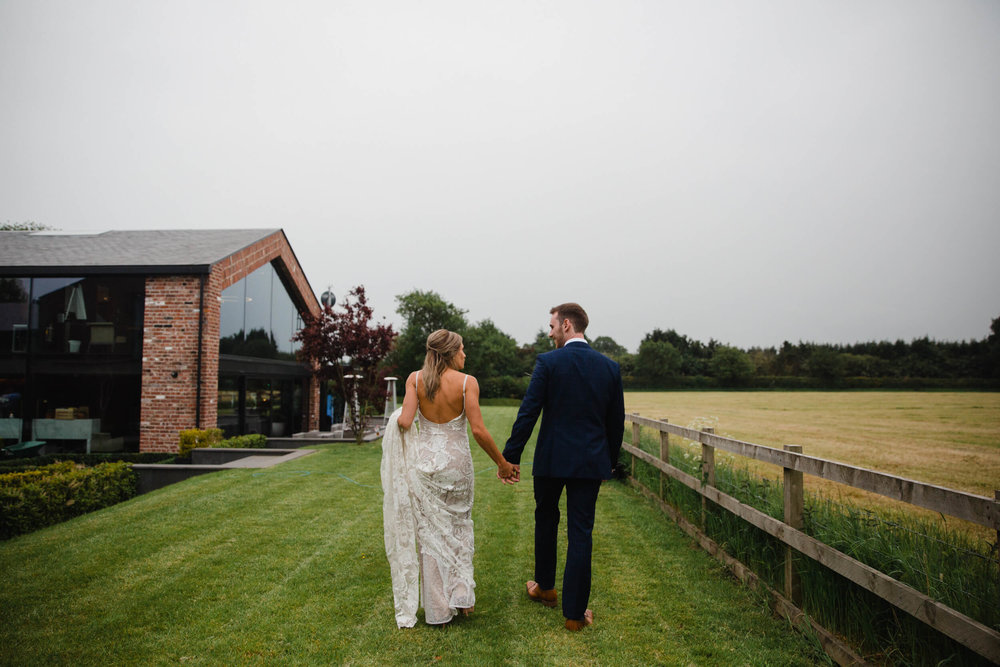 bride and groom holding hands and walking together away from camera